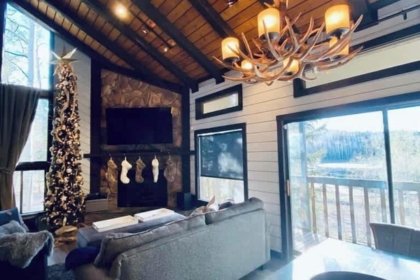 Step into a cozy mountain retreat where you can unwind by the stone fireplace and bask in the warmth of the rustic wood-beamed ceiling. The stunning chandelier and panoramic views create a perfect setting for relaxation.