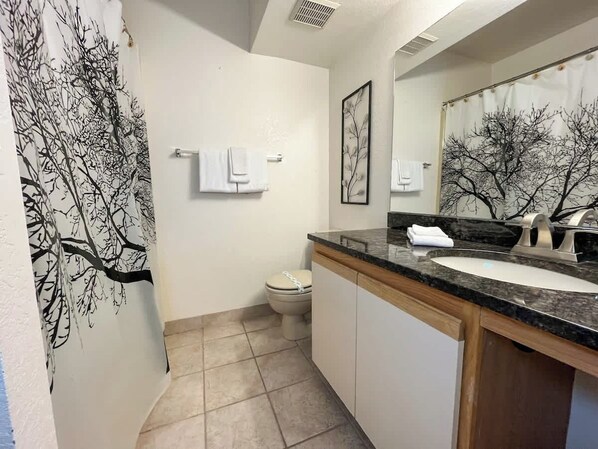 A bathroom with a toilet, sink, and a tree-themed shower curtain.