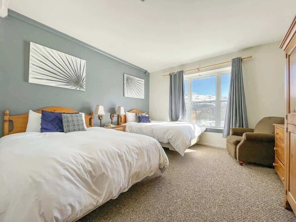 Une chambre d’hôtel avec deux lits, un bureau, une chaise et une vue sur l’extérieur.