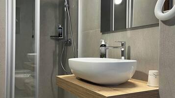 Ein modernes Badezimmer mit Duschkabine aus Glas, einem weißen Aufsatzwaschbecken und einer Holzwaschkommode.