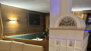 Uma sala de estar com sofá bege, mesa de centro de madeira, lareira com revestimento de azulejos e televisão fixada na parede.
