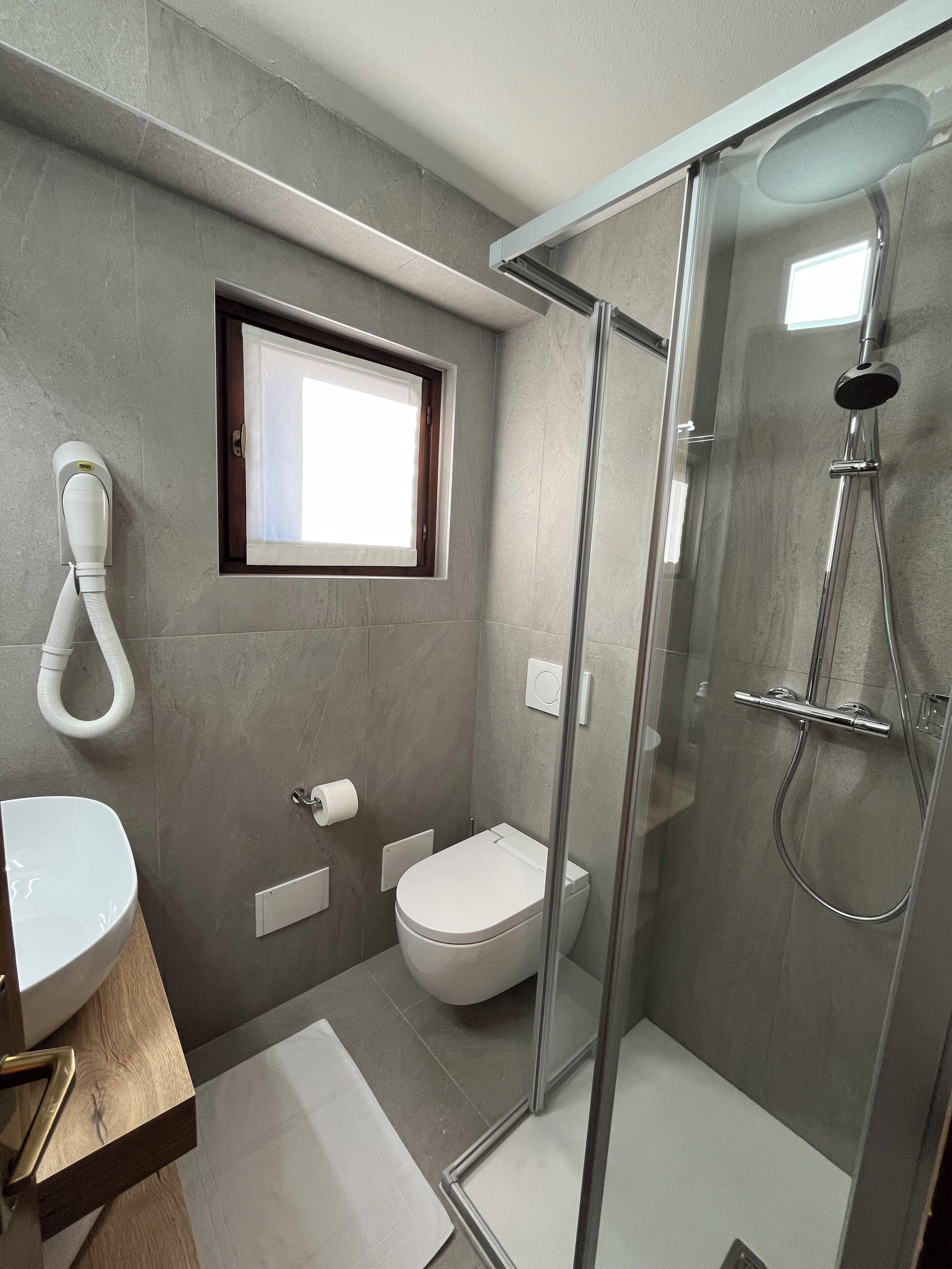 Ein modernes Badezimmer mit Duschkabine aus Glas, Toilette und Waschbecken mit Holzablage.