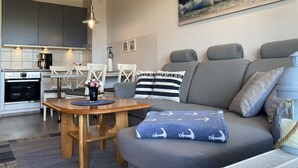 A modern living room with a grey sofa, a wooden coffee table, and a painting of a wave on the wall.