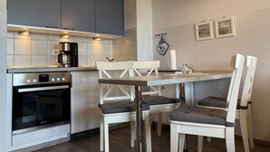 A modern kitchen with grey cabinets, a coffee maker, and a dining area with white chairs and a table.