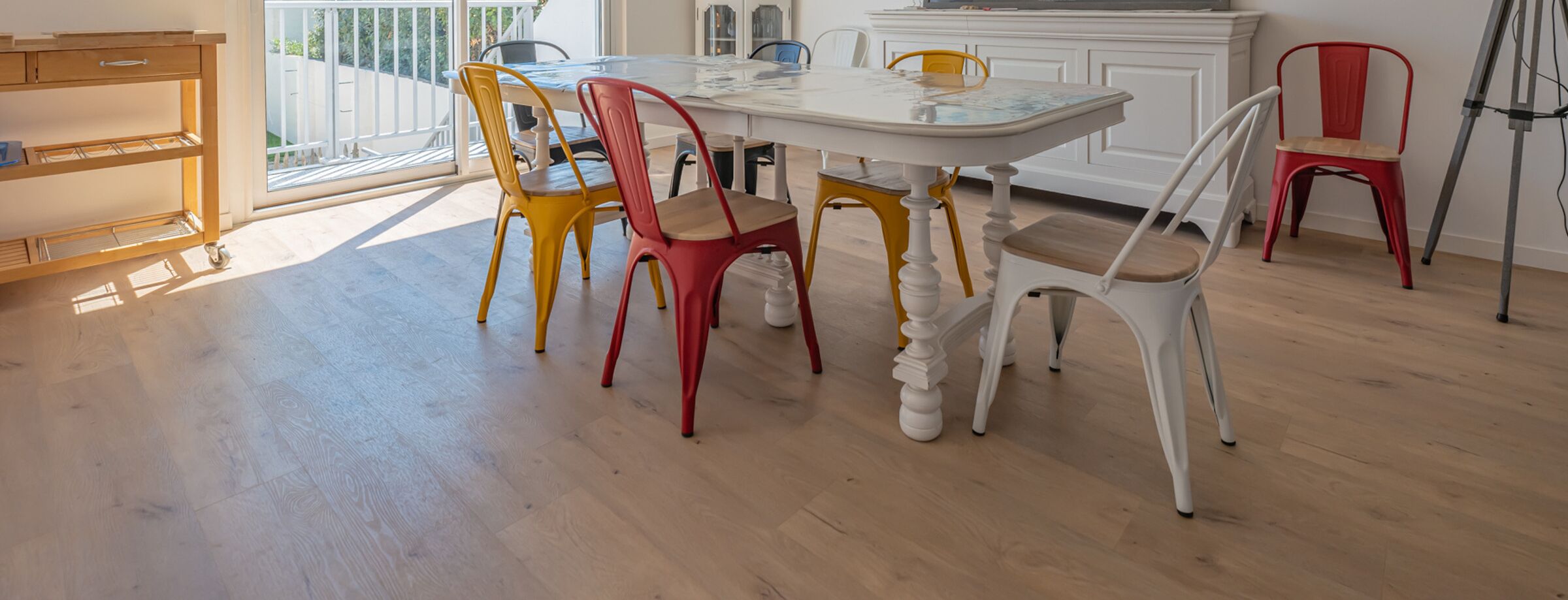 Een eetruimte met een witte tafel en kleurrijke stoelen, een houten kast, en uitzicht op de omgeving.