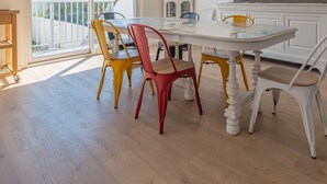 Een eetruimte met een witte tafel en kleurrijke stoelen, een houten kast, en uitzicht op de omgeving.