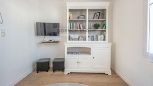 Een moderne woonkamer met een wit kastje, een flatscreen televisie en twee zwarte voetenbankjes.