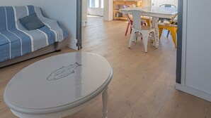 Een kamer met een gestreept bankje, een witte tafel met een vismotief en een houten vloer.