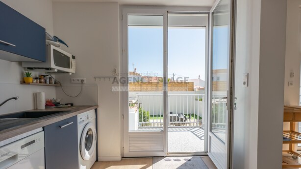 Een moderne keuken met een wasmachine, een magnetron en een spoelbak. Er is een schuifdeur naar een balkon met uitzicht op de omgeving.