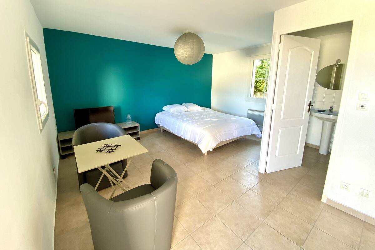 Un dormitorio con cama, escritorio y silla. Se ve un baño por una puerta abierta.