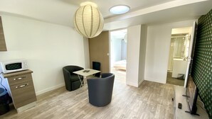 Una habitación moderna con piso de madera, una mesita, una silla, microondas, bote de basura y un ventanal grande.