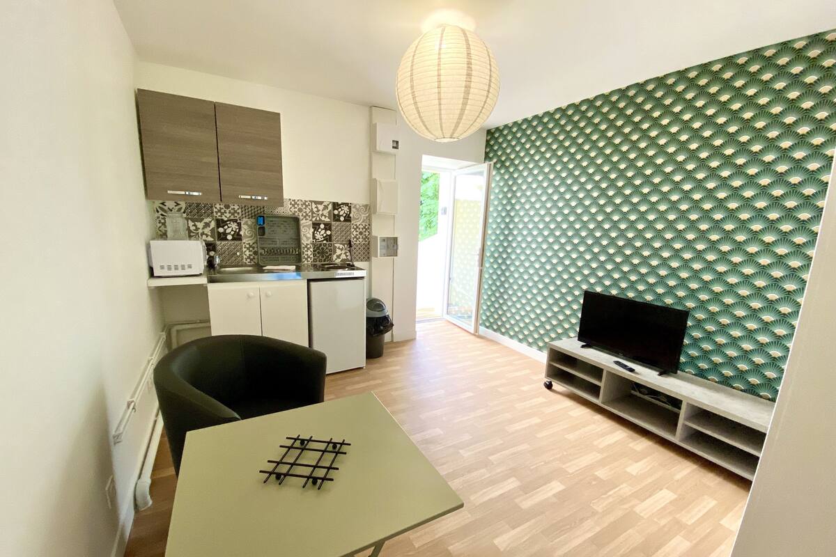 Una cocina compacta con electrodomésticos modernos, una mesa de comedor con estampado de cuadrícula y un televisor sobre un mueble.