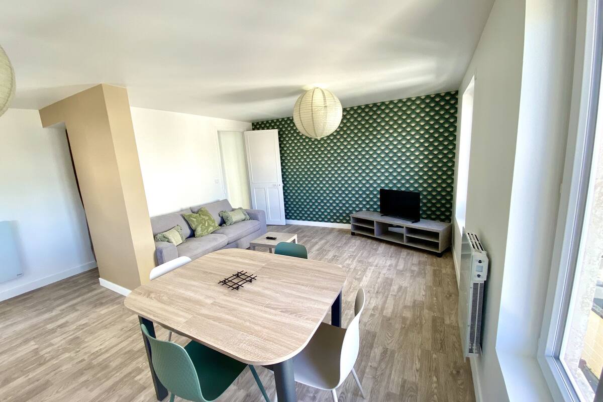 Una sala de estar moderna con un sofá, una mesa de comedor con sillas, un televisor sobre un mueble y una pared con diseño.