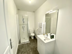 Et moderne badeværelse med bruseniche, toilet og hvid vask med spejl.