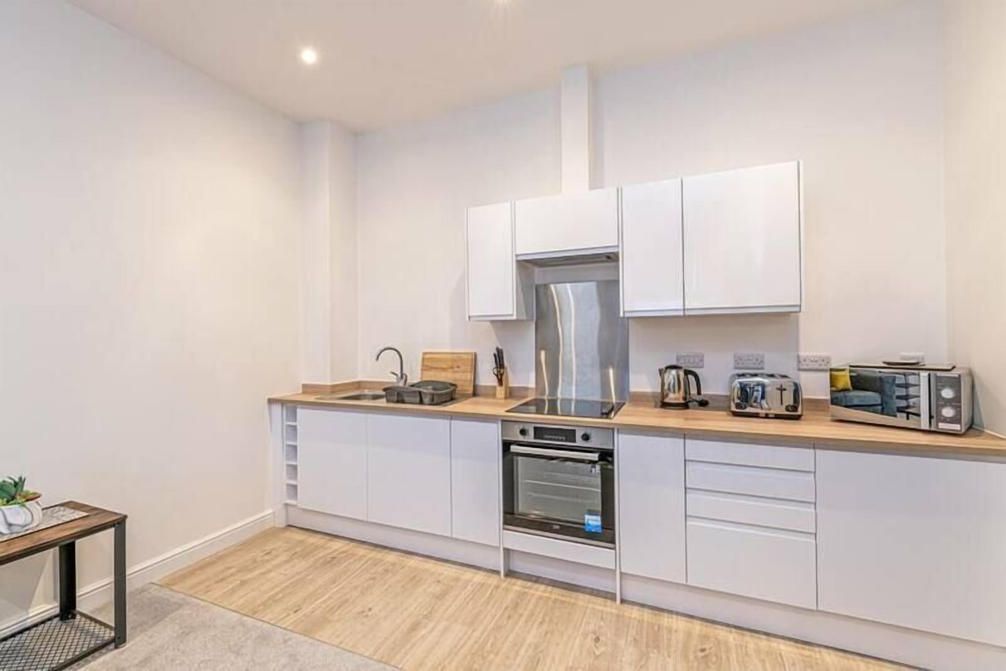A modern kitchen with white cabinets, a stainless steel range hood, a built-in oven, and a microwave.