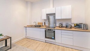 A modern kitchen with white cabinets, a stainless steel range hood, a built-in oven, and a microwave. - Prescott Court by Guestz (Halifax)