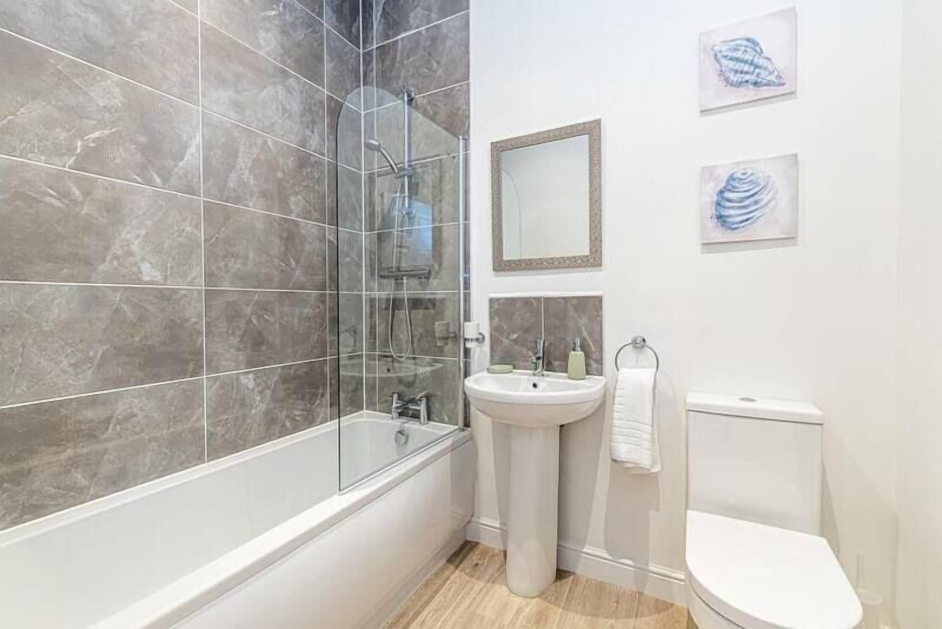 A modern bathroom with a glass-enclosed shower, a pedestal sink, and a toilet.