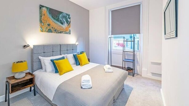 A modern bedroom with a large bed, a painting on the wall, and a window with a view. - Prescott Court by Guestz (Halifax)