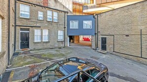 A narrow urban street with a parked car, brick buildings, and a modern glass structure. - Prescott Court by Guestz (Halifax)