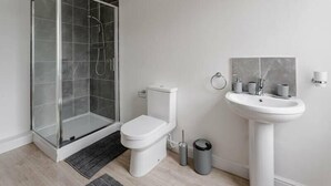 Un bagno moderno con box doccia in vetro, un water, un lavandino e un cestino.