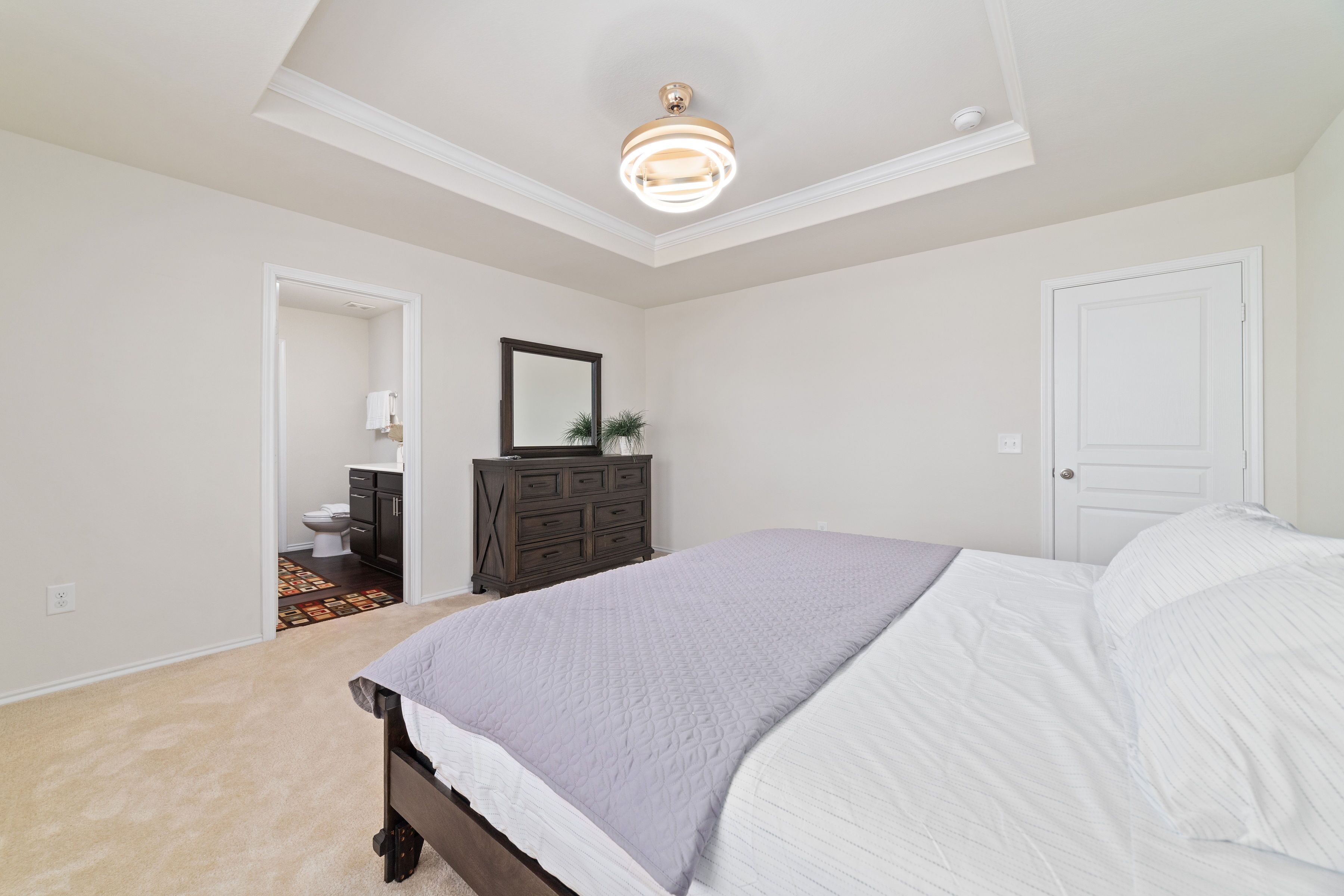 A bedroom with a bed, dresser, mirror, and a door.