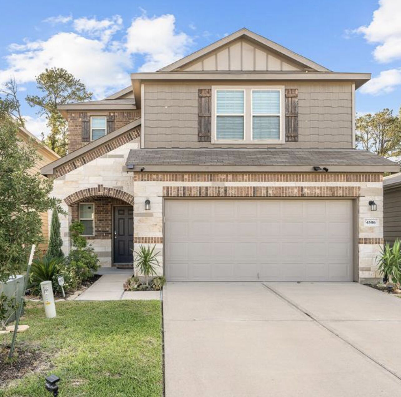 A two-story house with a garage, a brick entrance, and a well-maintained lawn.
