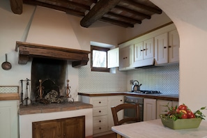 A kitchen with wooden beams, a stove, white cabinets, and a window.
