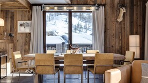 A cozy dining area with a wooden table and chairs, a mounted animal head on the wall, and a view of a snowy mountain landscape. - Luxury Apartment with Hammam, Fireplace, and Mountain View in Val d'Isère (Val-d'Isère)