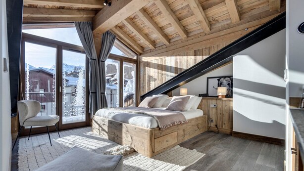 A bedroom with a wooden ceiling, a bed, a chair, and a view of snowy mountains through large windows. - Luxury Apartment with Hammam, Fireplace, and Mountain View in Val d'Isère (Val-d'Isère)