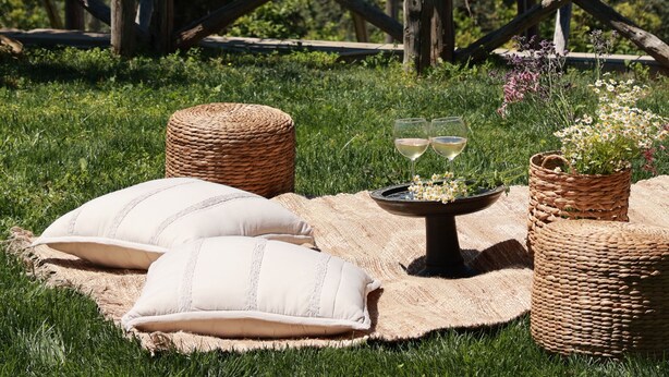 Un espacio al aire libre con césped, muebles de mimbre, una mesa con vasos y vistas al mar.