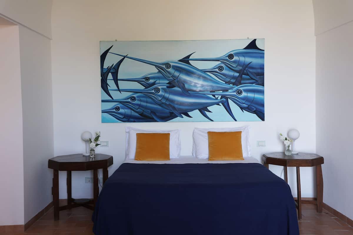 Une chambre à coucher avec un grand lit, deux tables de chevet et un tableau représentant des poissons, accroché au mur.