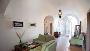 Un amplio salón con un conjunto de sofás verdes, una mesa de centro de madera y un gran ventanal arqueado que proporciona luz natural.