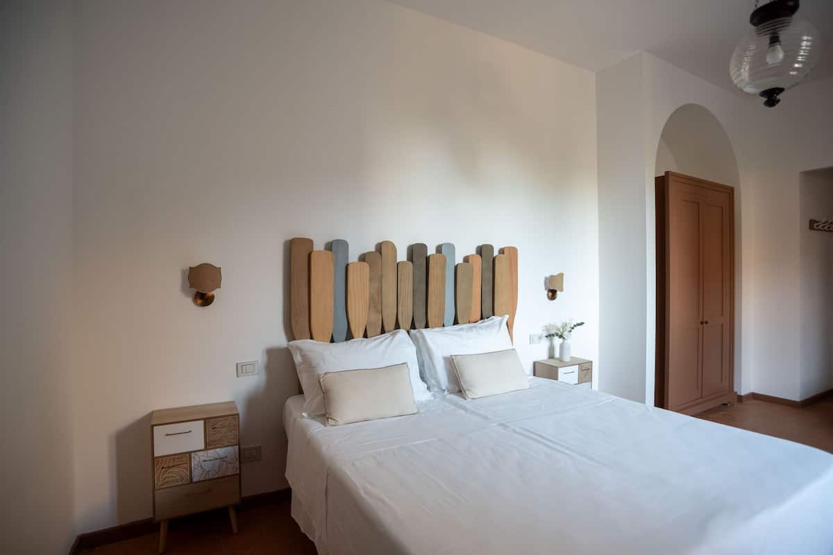 Une chambre à coucher comprenant un lit, une tête de lit en bois, des tables de chevet et une armoire.