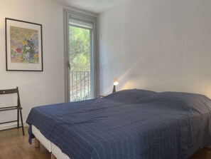 A bedroom with a bed, a chair, a window, and a nightstand with a lamp. - Renovated Apt with AC, parking & terrace 500m from the port (Banyuls-sur-Mer)