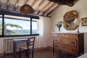 A room with a wooden desk, a chair, a dresser, a mirror, and a window with a view of trees and hills. - Entire home hosted by Agriturismo Castello Di Montozzi (Pergine Valdarno)