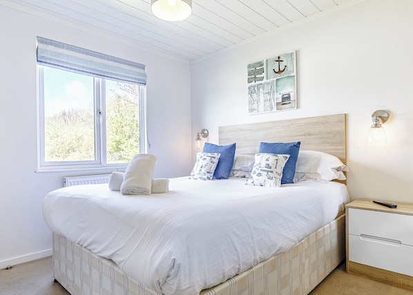 A bedroom with a large bed, a nightstand, a wall-mounted light, and a window with a view of trees.