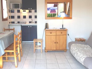 A compact living space with a kitchenette, a dining area, a small wooden cabinet, and a sofa. - Charming 2BR Pavilion with Pool Access, Terrace, and Parking, 400m from Sea (Gruissan)