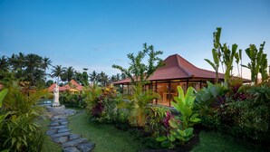 A tropical resort with a red-roofed building surrounded by lush greenery and a stone pathway. - Kampung Uma Dawa Villas and Spa (Ubud)