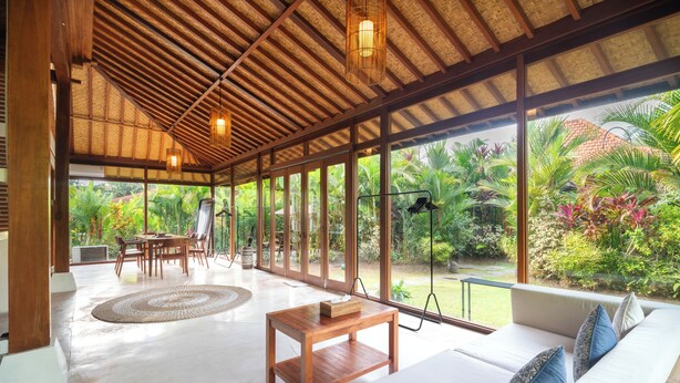 A spacious room with a wooden ceiling, large windows, a sofa, a table, and a dining area. - Kampung Uma Dawa Villas and Spa (Ubud)