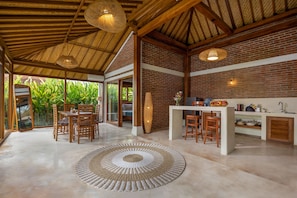 A spacious indoor area with a dining table and chairs, a kitchen counter, and a large woven rug. - Kampung Uma Dawa Villas and Spa (Ubud)