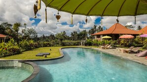 A pool area with lounge chairs and umbrellas, surrounded by lush greenery and a curved pool edge. - Kampung Uma Dawa Villas and Spa (Ubud)
