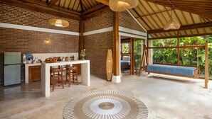 A spacious kitchen with a central island, a dining area with wooden chairs, and a hanging swing seat. - Kampung Uma Dawa Villas and Spa (Ubud)