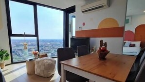 A modern room with a large window offering a city view, a wooden dining table, and a cozy seating area with a cushioned bench.