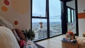 A modern living room with a large window offering a city view, a sofa, and a small table with a vase.