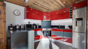 Une cuisine moderne avec des meubles de rangement rouges et gris, des appareils électroménagers en acier inoxydable et un plafond en bois.