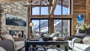 Un salon chaleureux avec un mur en pierre, une cheminée et une grande fenêtre donnant sur une montagne enneigée.