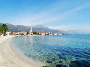 A coastal town with a clear beach, calm sea, and historic buildings.