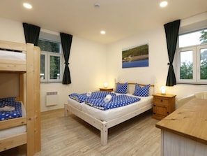 A bedroom with a bunk bed, a single bed, a wooden desk, and a window with curtains.
