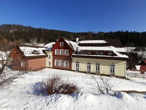 A two-story house with a red roof and beige walls, surrounded by snow-covered ground and trees. - Čertova hora by Interhome (Desná v Jizerských horách)