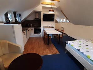 A compact kitchen with a dining area, a sofa, and a bed in a small attic room. - Čertova hora by Interhome (Desná v Jizerských horách)